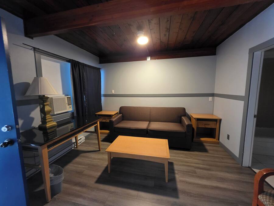 A small, cozy room with a wooden ceiling, a sofa, a coffee table, a TV, and a lamp.