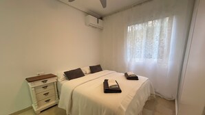Une chambre à coucher avec un lit, une table de chevet, une commode et une fenêtre avec des rideaux.