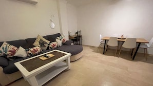 Un salon comprenant un canapé, une table basse, une table à manger avec des chaises et un miroir fixé au mur.