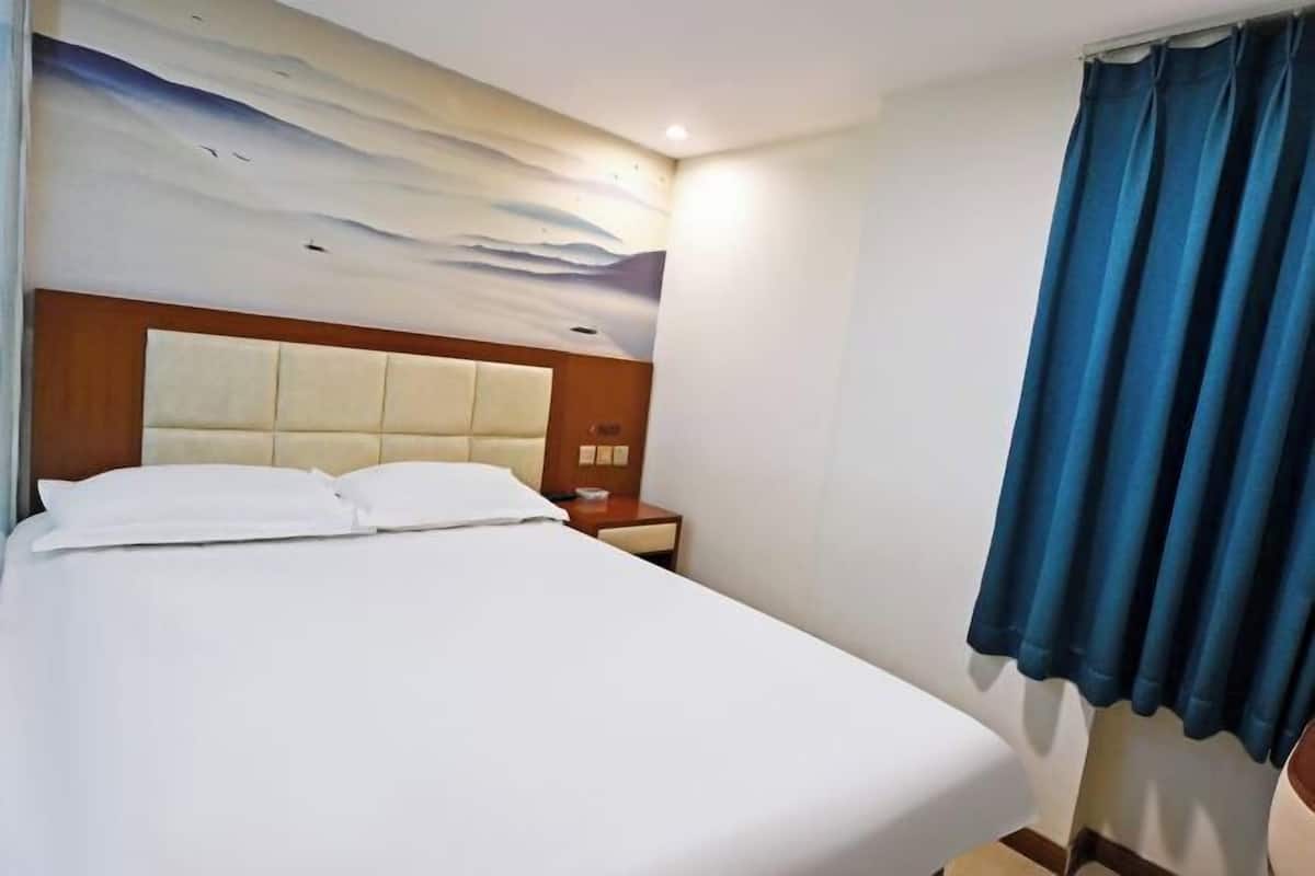 A hotel room with a large bed, a wooden headboard, a nightstand, and a blue curtain.