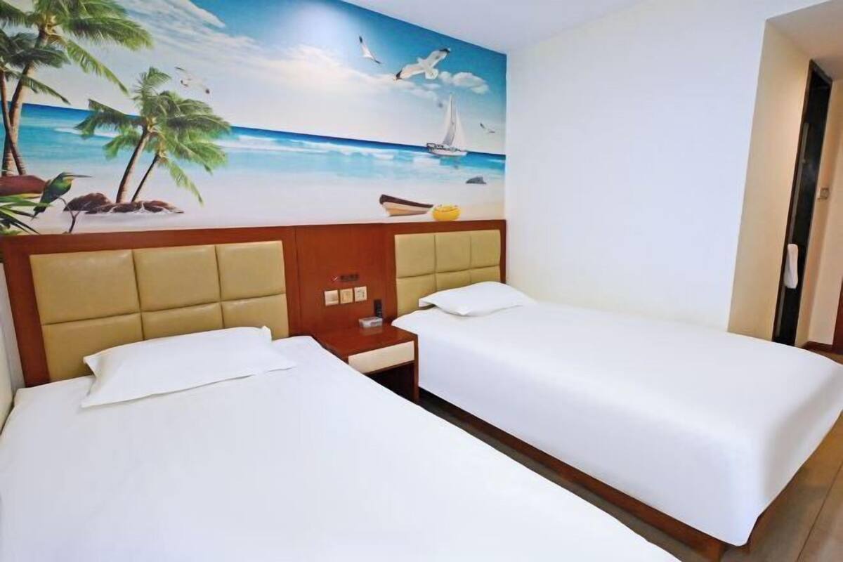 A hotel room with two beds, a wooden headboard, a nightstand, and a mural of a beach scene.