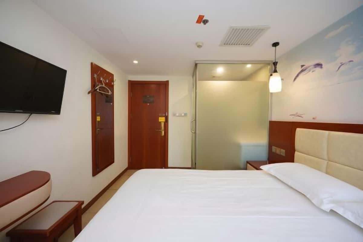 A hotel room with a bed, a television mounted on the wall, a door with a coat rack, and a shower area.