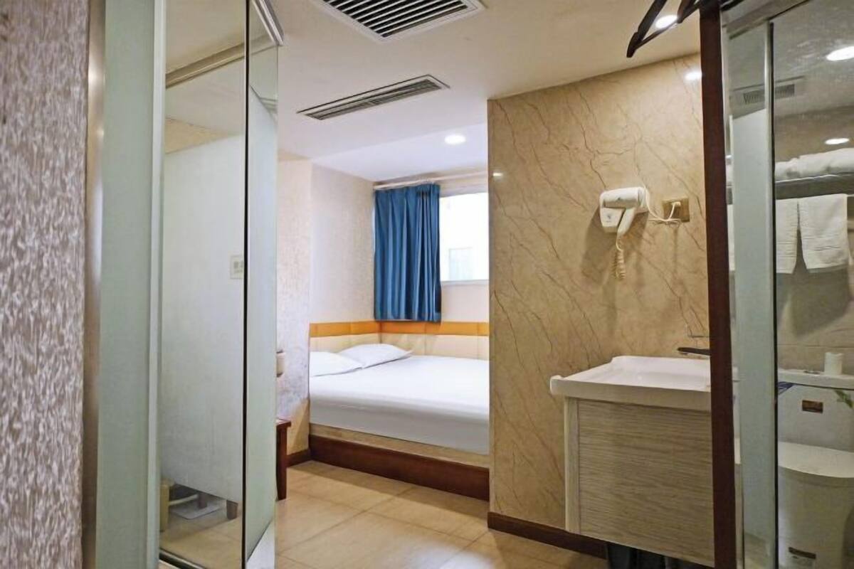 A hotel room with a bed, a bathroom with a sink and mirror, and a window with curtains.