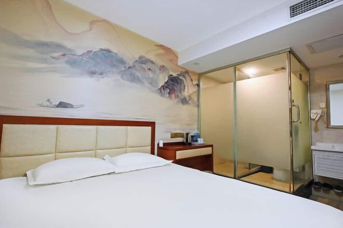 A hotel room with a bed, a nightstand, a glass-enclosed walk-in closet, and a bathroom with a sink and mirror.