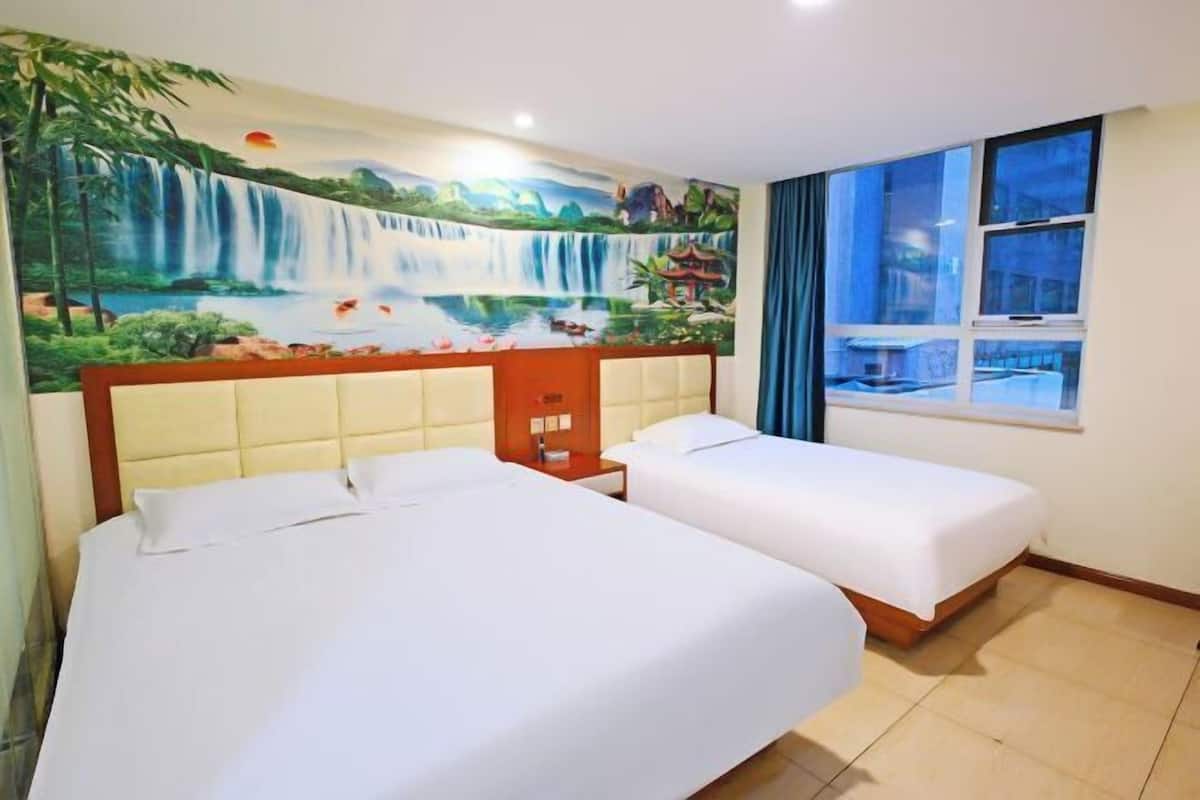 A hotel room with two beds, a mural of a waterfall, a window with curtains, and a wooden cabinet.