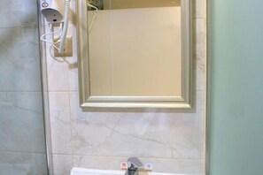 Une salle de bain avec un mur en marbre, un miroir, un lavabo et un sèche-cheveux posé sur un support mural.