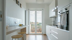 A modern kitchen with white cabinets, a built-in oven, and a large window overlooking a balcony. - Between sea and city, 15 minutes from the airport, 5 minutes from the excavations of Ostia Antina, (Lazio)