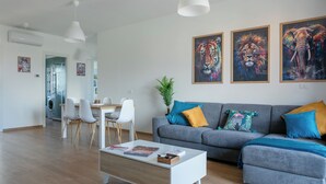 A modern living room with a grey sofa, white coffee table, and a dining area with chairs and a table. There are three framed animal paintings on the wall. - Between sea and city, 15 minutes from the airport, 5 minutes from the excavations of Ostia Antina, (Lazio)