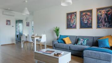 A modern living room with a grey sofa, white coffee table, and a dining area with chairs and a table. There are three framed animal paintings on the wall.