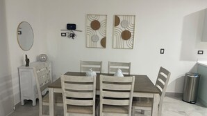 Een eetruimte met een rechthoekige tafel, vier houten stoelen, een wit kastje, een spiegel en twee decoratieve wandpanelen.