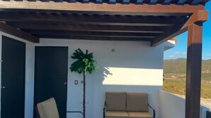 Een overdekt balkon met een bank en stoelen, een potplant en uitzicht op het landschap.
