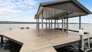 A wooden dock extending into a calm body of water, with a covered seating area and a view of distant hills. - Lakefront 6BR Retreat with Private Dock, Huge Deck & Epic Seneca Views (Dundee)
