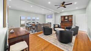 A spacious living area with a wooden floor, a ceiling fan, and a view through large windows. - Lakefront 6BR Retreat with Private Dock, Huge Deck & Epic Seneca Views (Dundee)