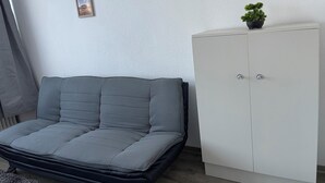 Huoneessa on harmaa sohva, valkoinen vaatekaappi ja seinällä kolme kehystettyä kuvaa.