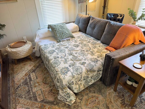 A cozy bedroom with a bed, a wooden side table, and a patterned rug.