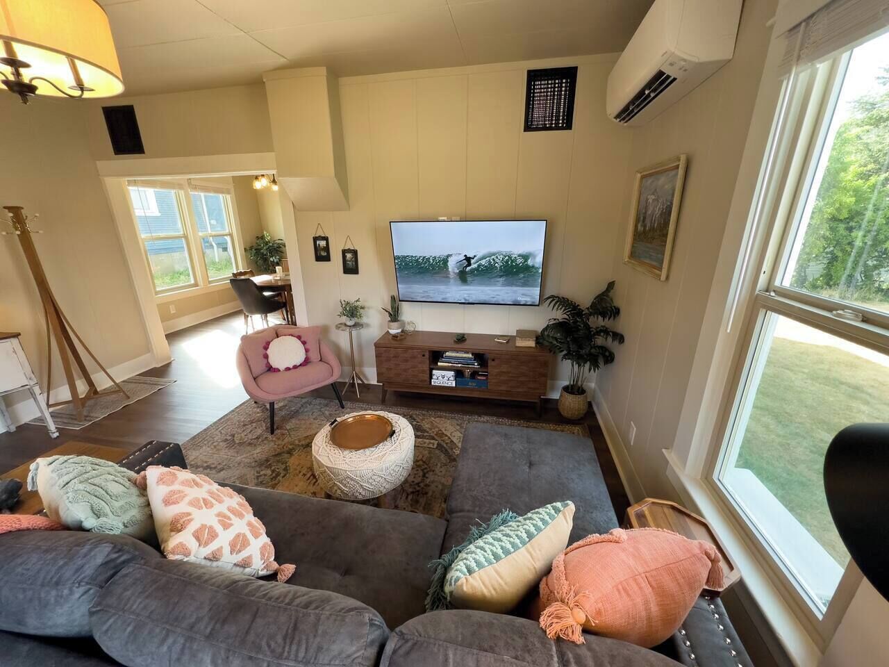 A living room with a large flat-screen TV, a gray sofa, a pink chair, and a wooden coffee table.