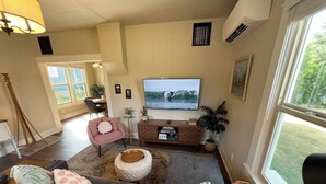 Ein Wohnzimmer mit einem großen Flachbildfernseher, einem grauen Sofa, einem rosafarbenen Sessel und einem Holztisch.