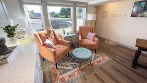 A modern living room with two peach-colored armchairs, a round ottoman, and a patterned rug. - Downtown Studio | Small + Stylish | Near WWU (Bellingham)