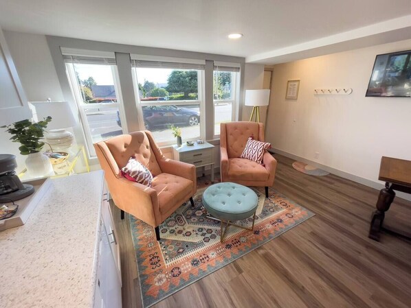 A modern living room with two peach-colored armchairs, a round ottoman, and a patterned rug.