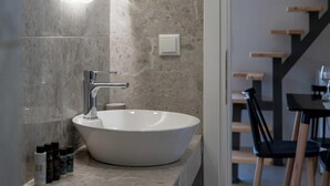 Une salle de bain moderne avec un grand lavabo sur pied blanc, un luminaire fixé au mur et un escalier en bois en arrière-plan.