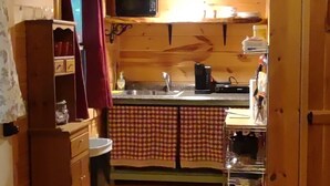 A compact kitchen with wooden walls, a checkered backsplash, a sink, a microwave, and a coffee maker. - Pine Ridge Cabin - A Cozy Getaway for Two near Jasper AR! (Jasper)
