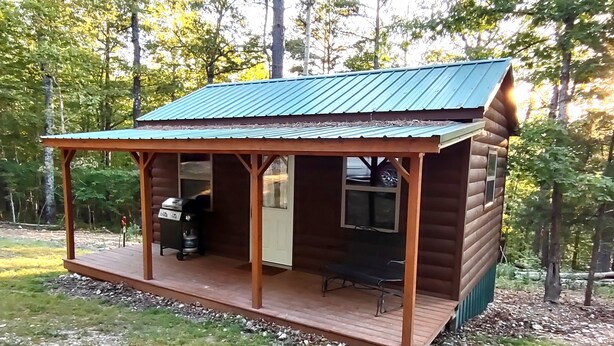 A wooden cabin with a porch, a grill, and a bench. - Pine Ridge Cabin - A Cozy Getaway for Two near Jasper AR! (Jasper)