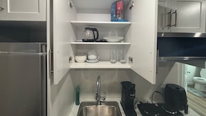 A compact kitchen with a stainless steel sink, a kettle, and a coffee maker on the countertop. - The Snug Spot,Retreat offers a warm and inviting escape for travelers. (Winnipeg)