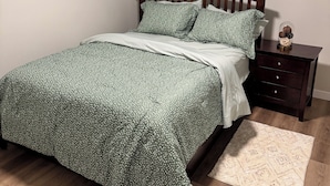 A bedroom with a bed, a nightstand, a dresser, a window with a view, and a ceiling light. - The Snug Spot,Retreat offers a warm and inviting escape for travelers. (Winnipeg)