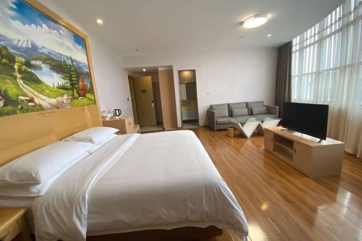 A hotel room with a bed, a sofa, a TV, and a painting on the wall.