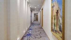 A hallway with a floral carpet design, a large framed painting on the right wall, and a door at the end. - Vienna Classic Hotel (Nanjing Nanzhan Jiangning Wanda Plaza) (Nanjing)