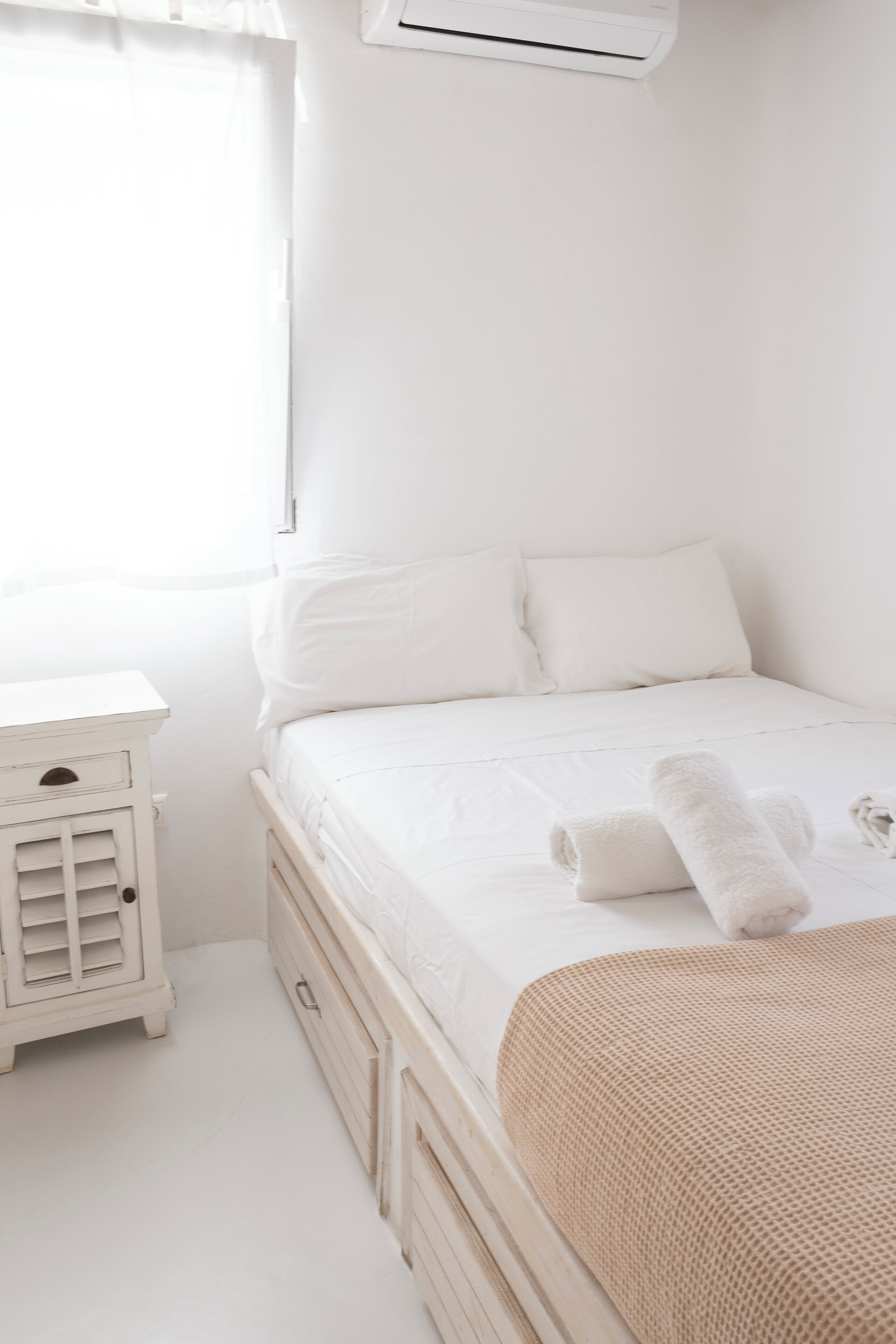 Une chambre à coucher blanche, avec un lit, une table de chevet et un appareil de climatisation.