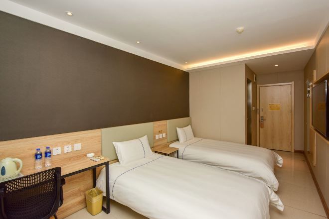 A hotel room with two beds, a desk with a chair, a TV, and a door.