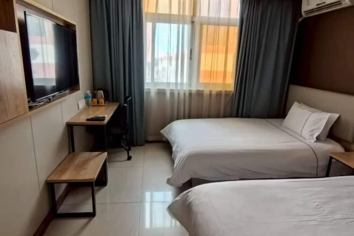 A hotel room with two beds, a desk, a TV, and a window with curtains.
