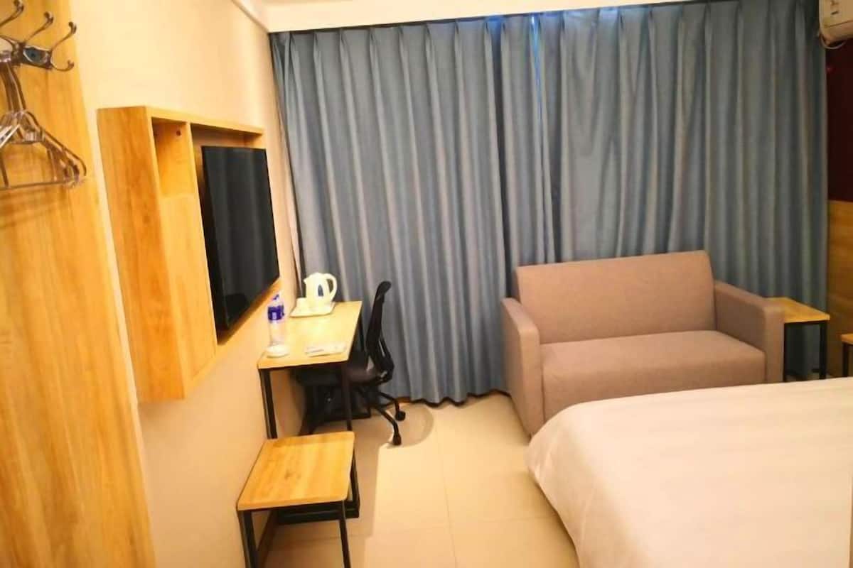 A hotel room with a bed, a desk with a chair, a sofa, a TV, and a curtain.