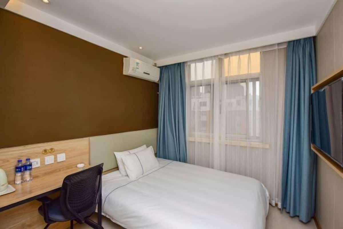 A hotel room with a bed, a desk with a chair, a TV, and a window with curtains.