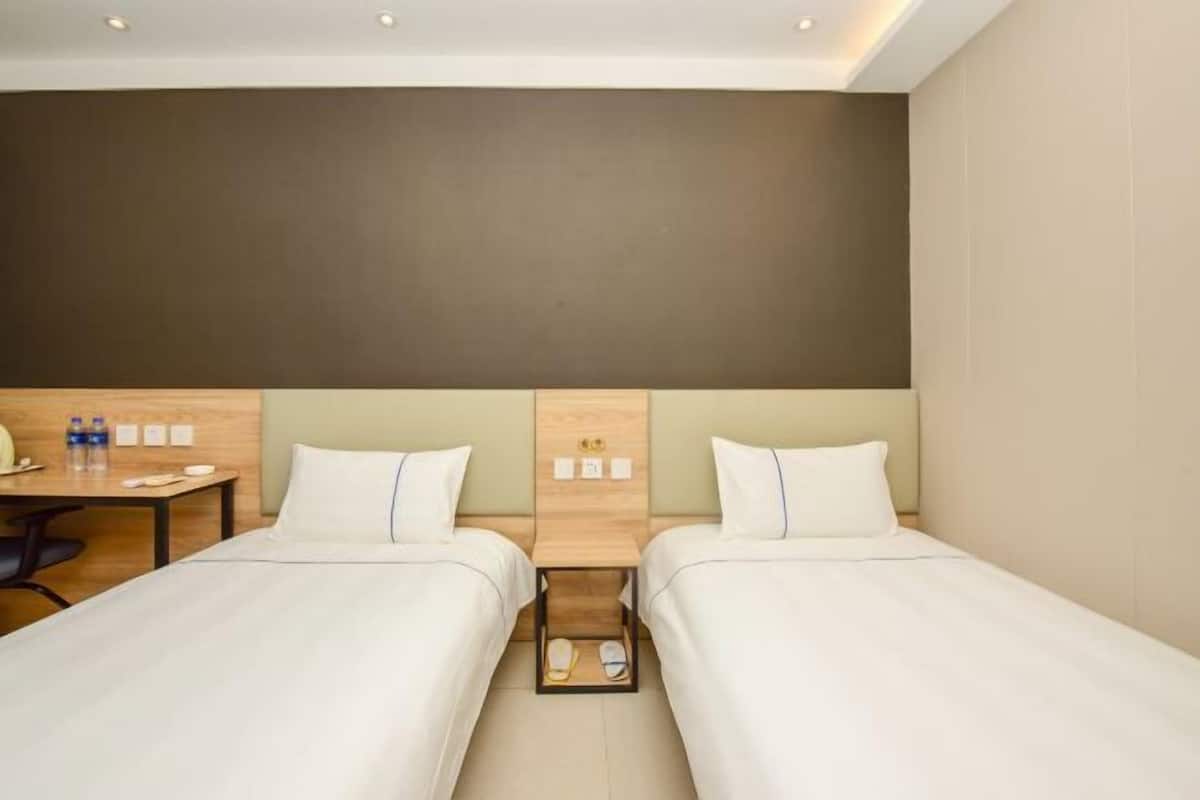 A hotel room with two beds, a wooden headboard, a small table with a chair, and a desk with a chair.