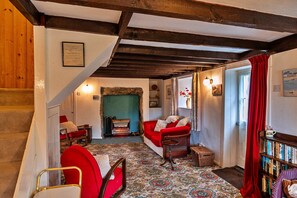 A cozy room with a staircase, a red sofa, a fireplace, and a bookshelf. - Cottage in Sennen Cove With Stunning Sea Views (Penzance)