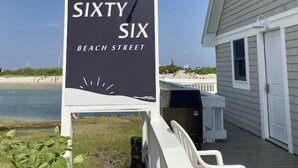 En skylt med texten ”Sixty Six Beach Street”, med utsikt över stranden och ett hus i bakgrunden.