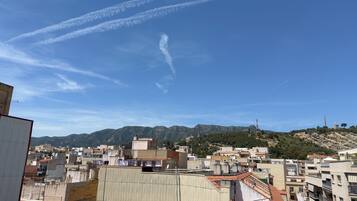 A cityscape with buildings, a mountain in the background, and contrails in the sky.