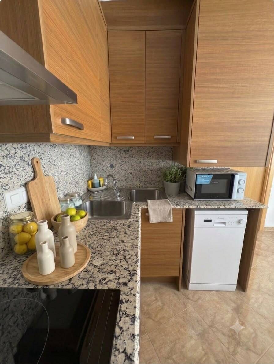 Une cuisine de taille réduite, dotée d’armoires en bois, d’un plan de travail en granit, d’un four à micro-ondes, d’un évier et d’un lave-vaisselle.