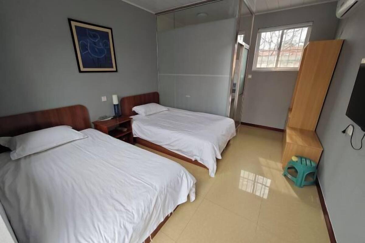 A hotel room with two beds, a wooden headboard, a window, and a wall-mounted TV.