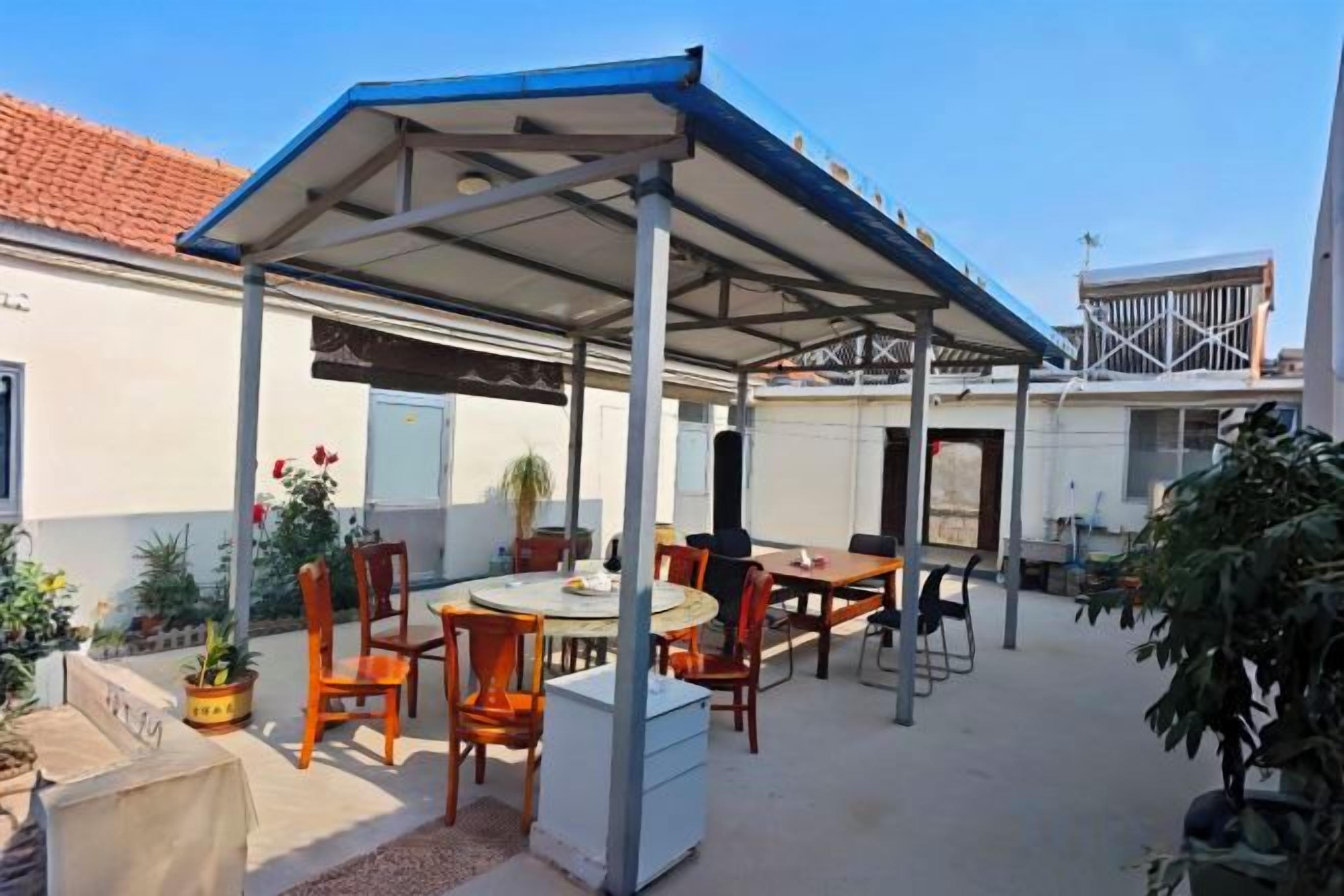 Un patio exterior con una zona de estar techada, mesas y sillas.