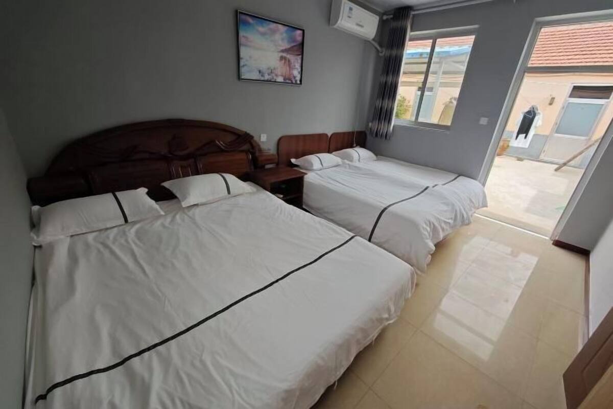 A hotel room with two beds, a wooden headboard, a nightstand, a painting, and a view of the outside.