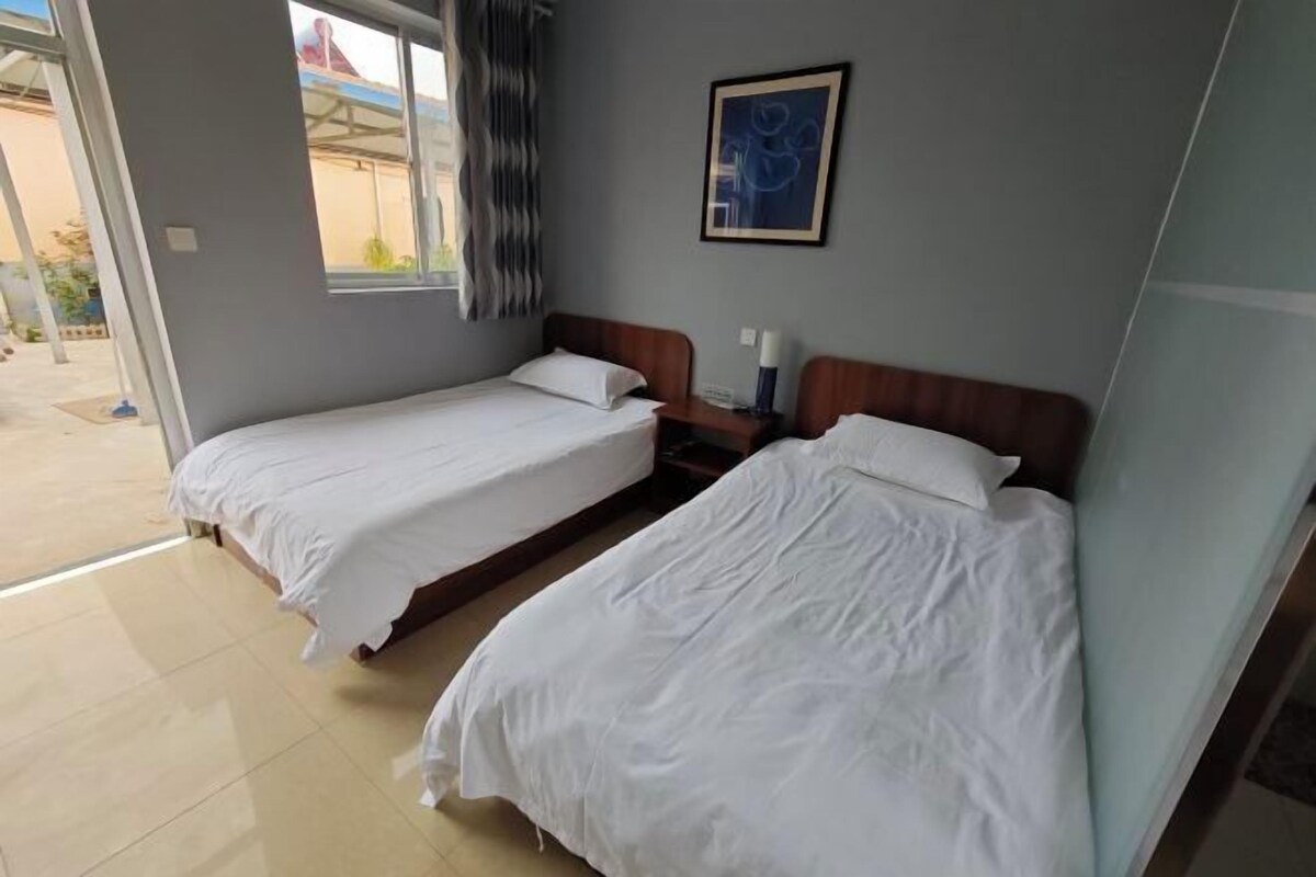 A hotel room with two single beds, a small table, and a window with curtains.