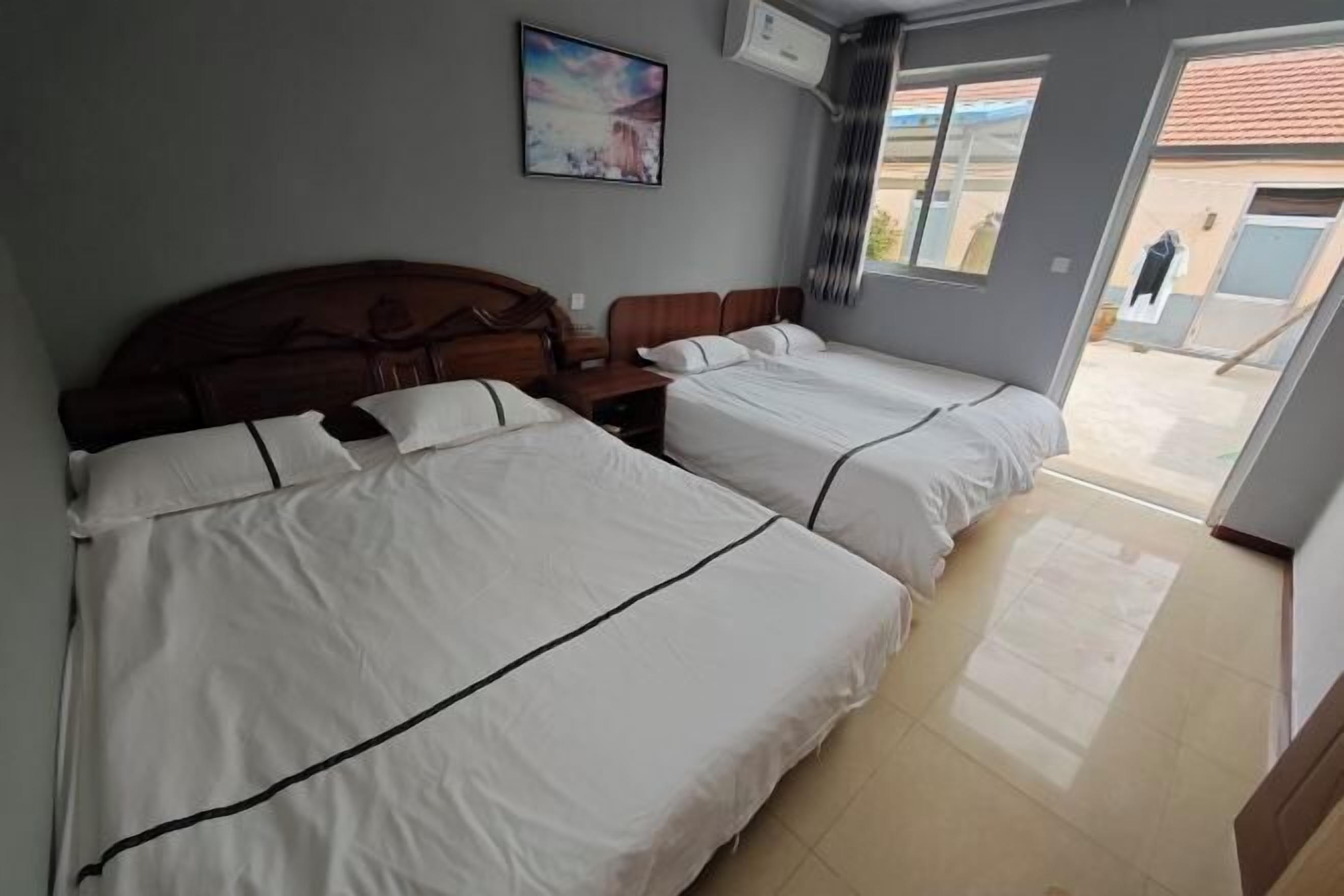 A hotel room with two beds, a wooden headboard, a painting on the wall, and a view of the outside.