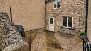 A stone cottage with a door, a window, and a small patio area with a table and chairs. - Cottage in Bradwell Near Peak Cavern (Hope Valley)