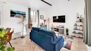 Un salon moderne avec un canapé bleu, un téléviseur à écran plat, un plancher en bois et une grande fenêtre avec des rideaux.