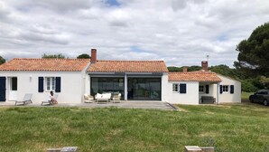 Une maison à deux étages, avec un toit en tuiles, une terrasse couverte et une cour gazonnée.