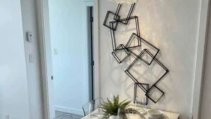 Ein moderner Essbereich mit einem rechteckigen Tisch, gedeckt für vier Personen, umgeben von Metallstühlen. Eine dekorative geometrische Leuchte hängt über dem Tisch, und in der Mitte des Tisches steht ein kleiner Topfpflanze.