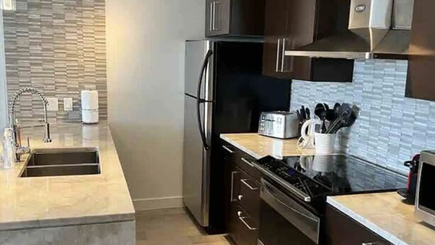 Eine moderne Küche mit dunklen Schränken, einem Edelstahlkühlschrank, einem eingebauten Ofen und einer Arbeitsplatte mit einem Toaster.